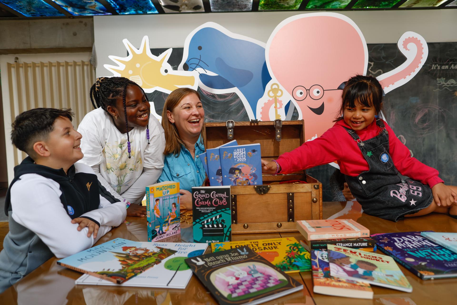 Young girl reaches for the Best Irish Books reading guide in the treasure chest, while young girl, young boy and woman look on