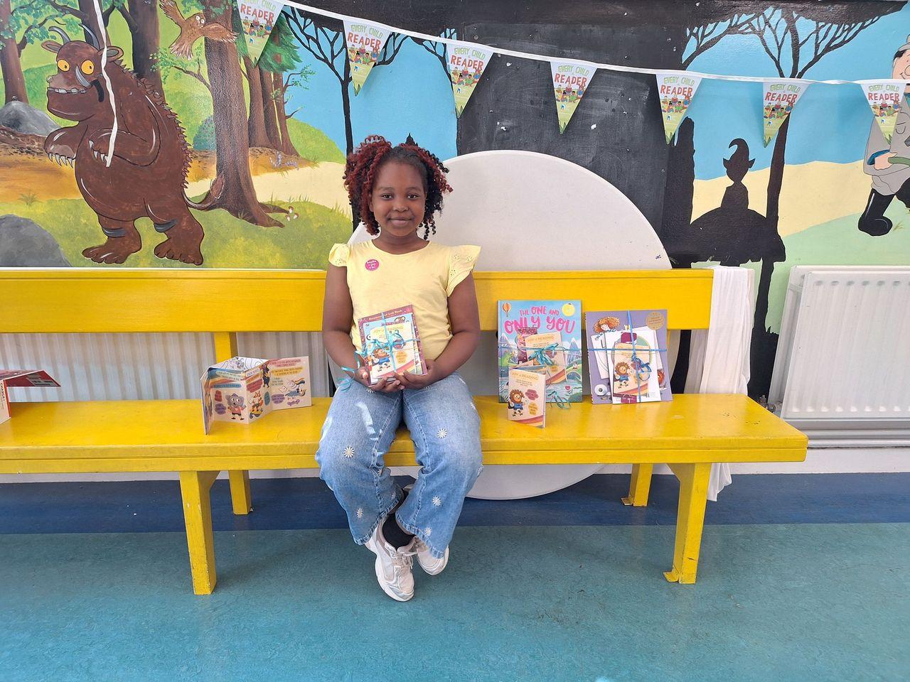 Little girl sitting on yellow bench and holding a book
