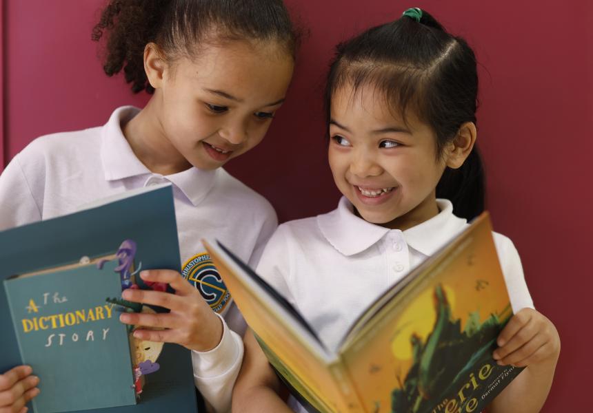 pink background two young girls stand side by side smiling with their new books
