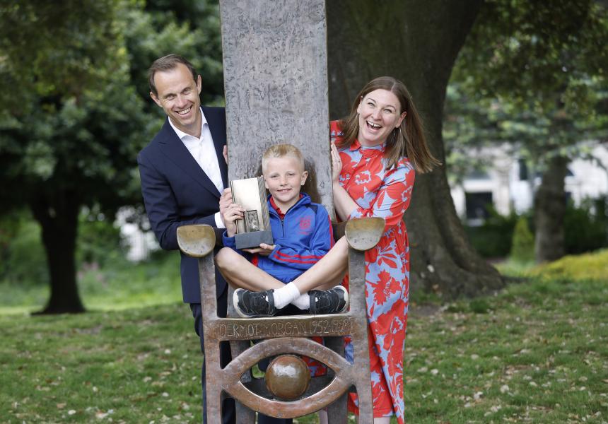 Child on metal chair with man and woman peeking out the sides