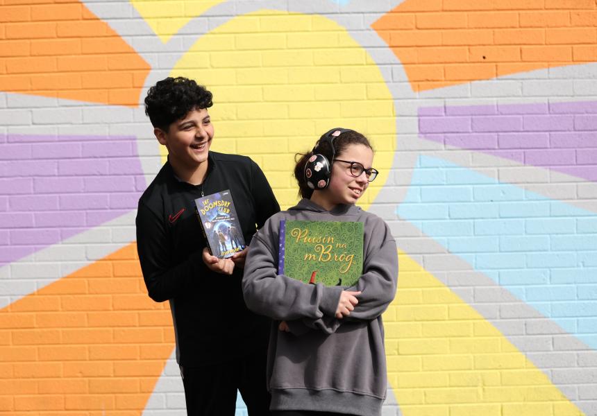 Students of Paradise Place pose in front of a sun mural while holding books